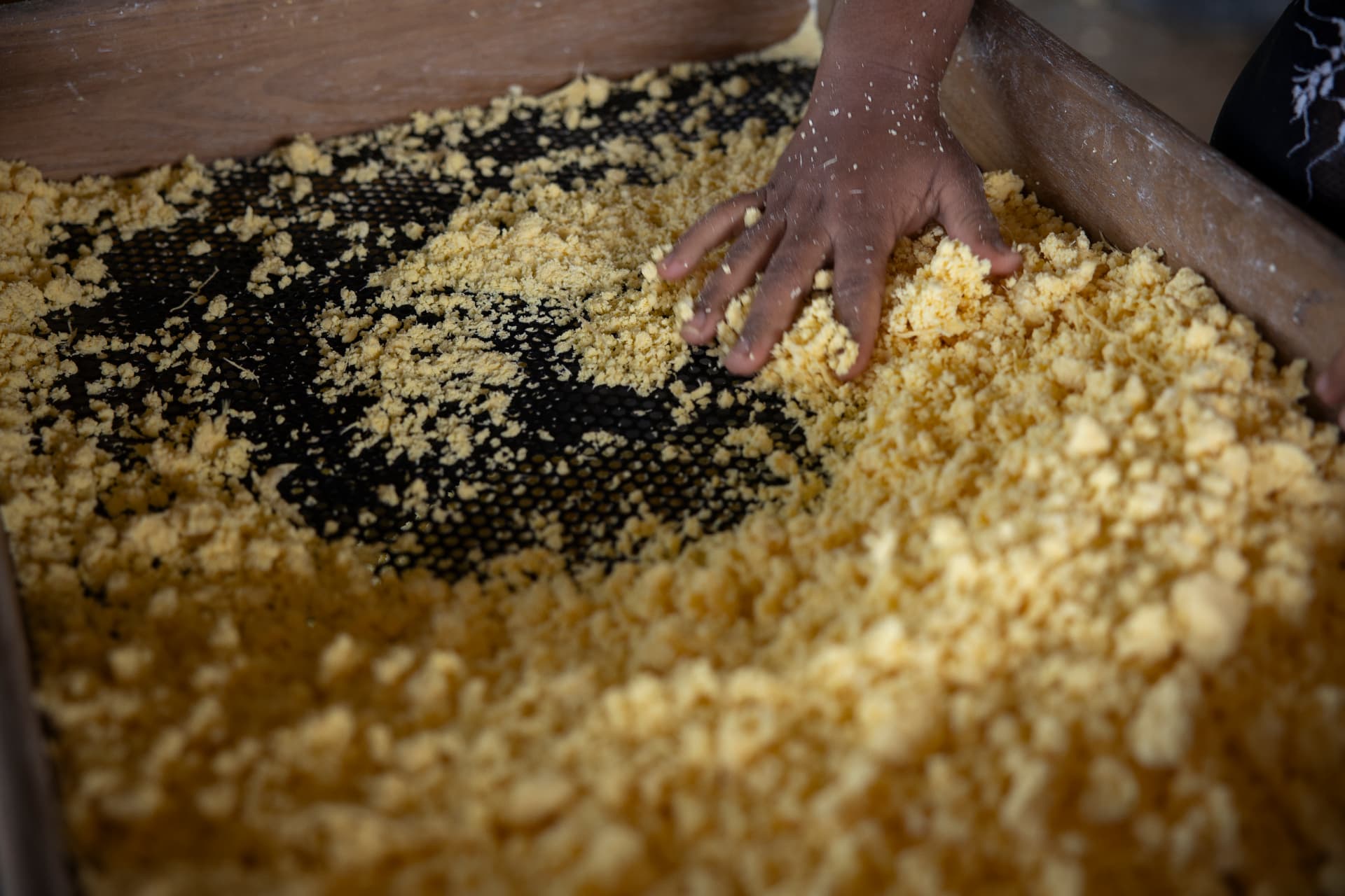 Produção artesanal de farinha de mandioca sendo peneirada à mão