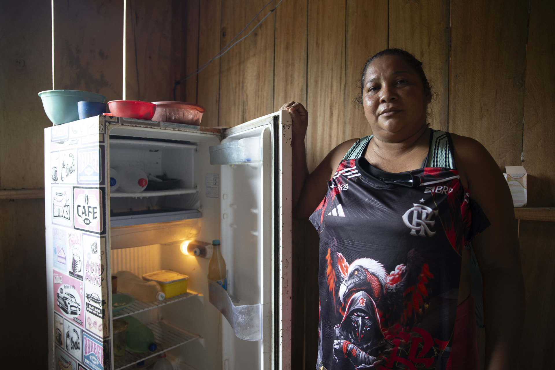 Moradora ao lado de sua geladeira ligada, dentro de casa em comunidade amazônica