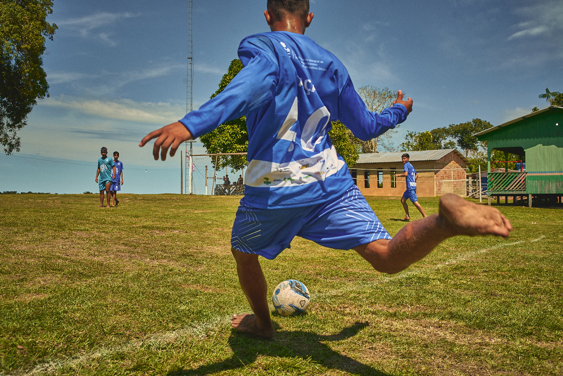 Menino chutando bola em campo de comunidade amazônica durante atividade esportiva