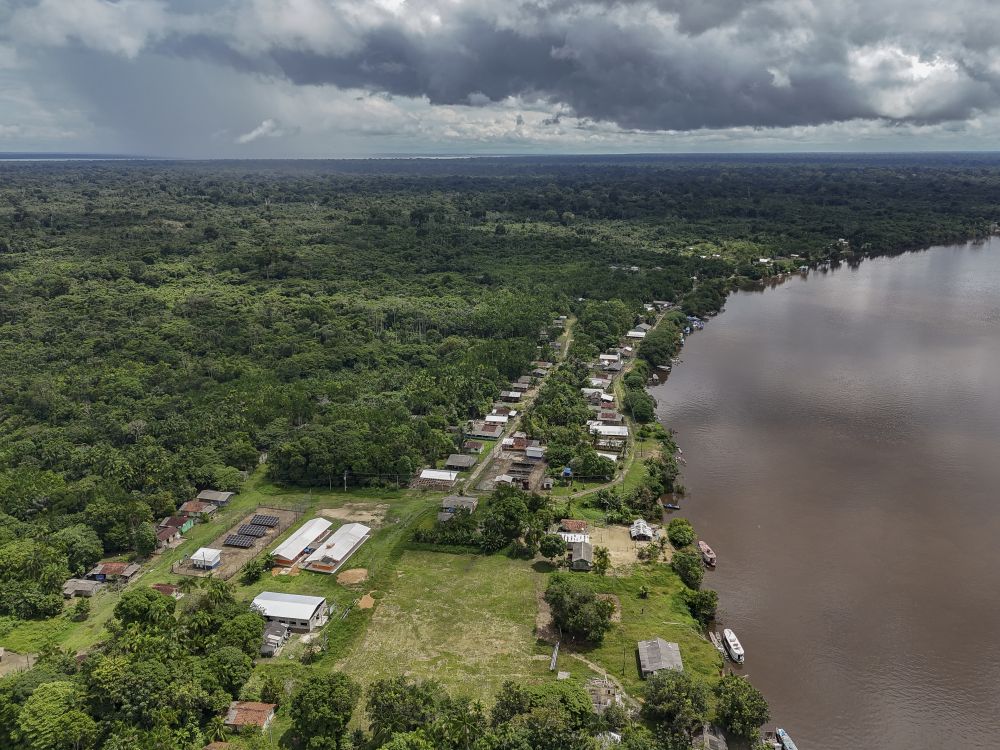 Vista aérea de comunidade ribeirinha às margens do rio, com floresta ao redor