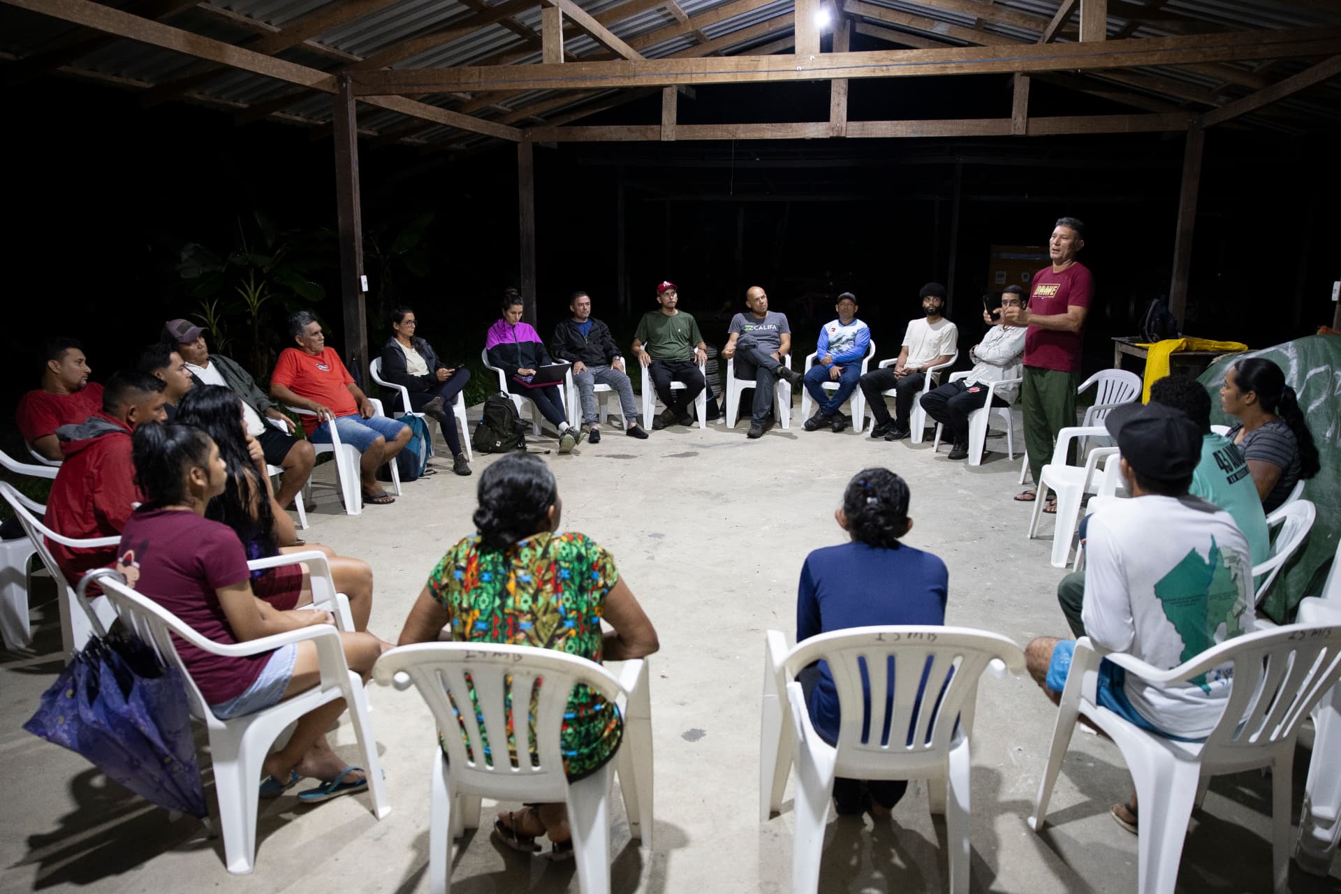 Moradores reunidos em roda durante assembleia comunitária à noite