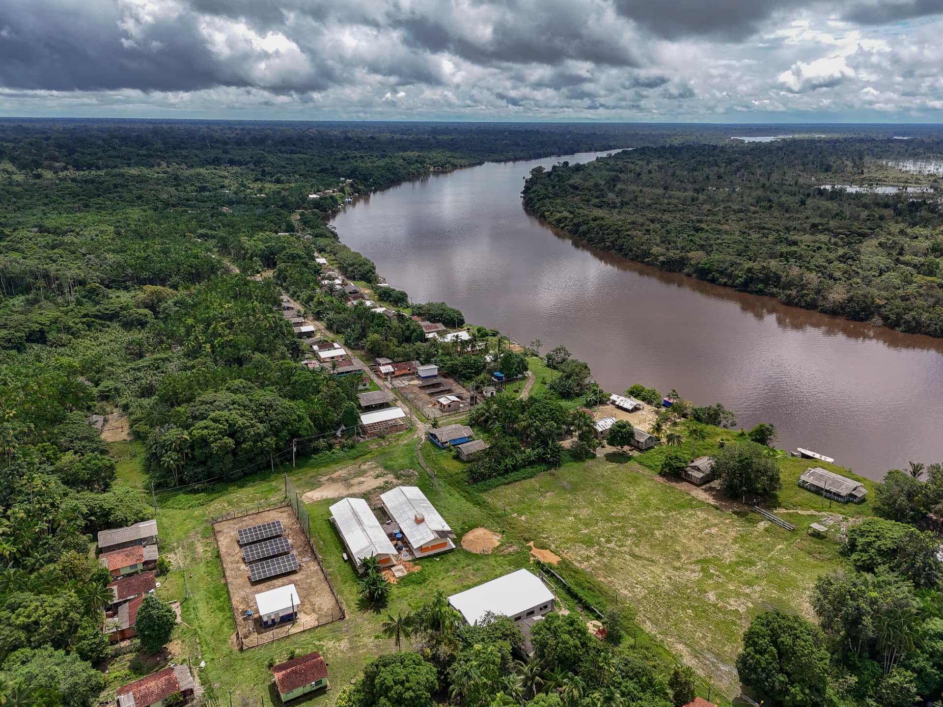 Vista aérea de comunidade ribeirinha com escola e sistema solar às margens do rio